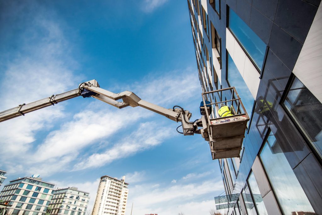 Construction worker on a lift near high-rise building against blue sky.