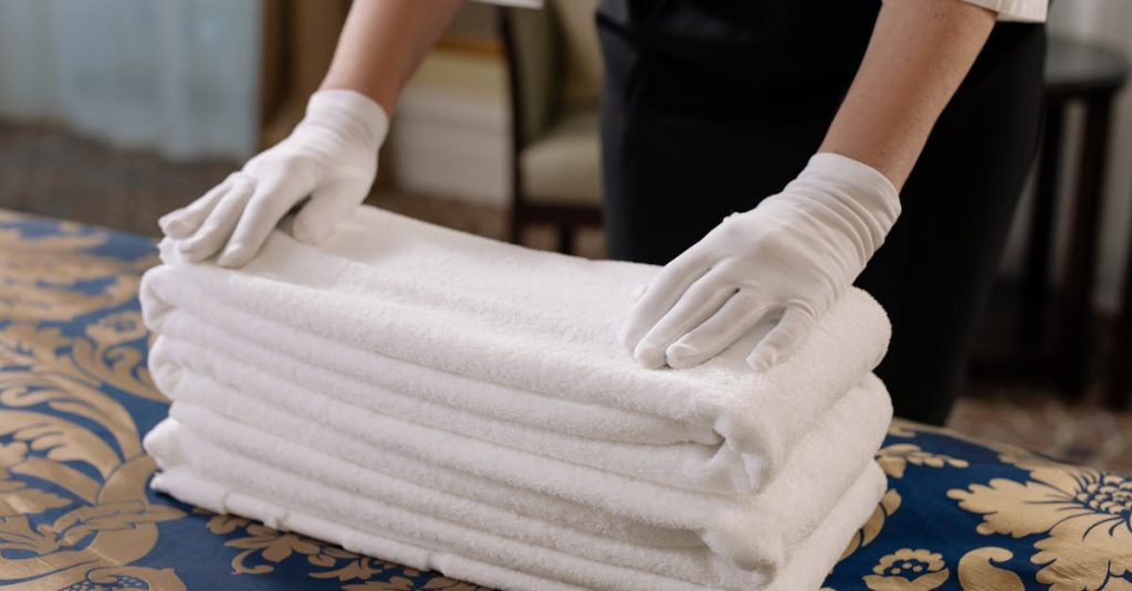 Professional housekeeper folding clean towels on a bed in a hotel room, emphasizing neatness and service.